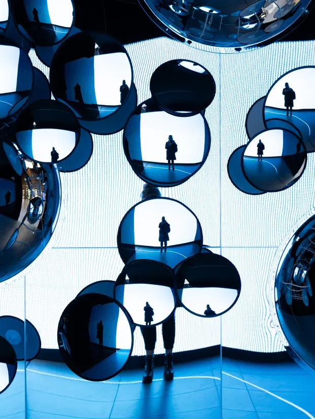 Interactive installation with mirrored spheres of different sizes in a blue illuminated space. A person’s silhouette is reflected across the mirrors, creating multiple perspectives and illustrating the value of choice and new viewpoints in MBA studies.