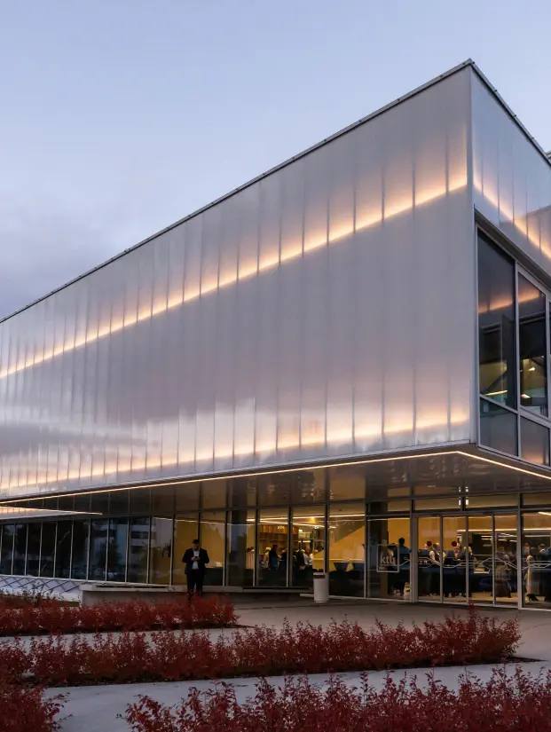 Modern KTU building in the evening with an illuminated facade and large glass windows. People gathered inside are visible through the windows, reflecting the active KTU MBA study environment.