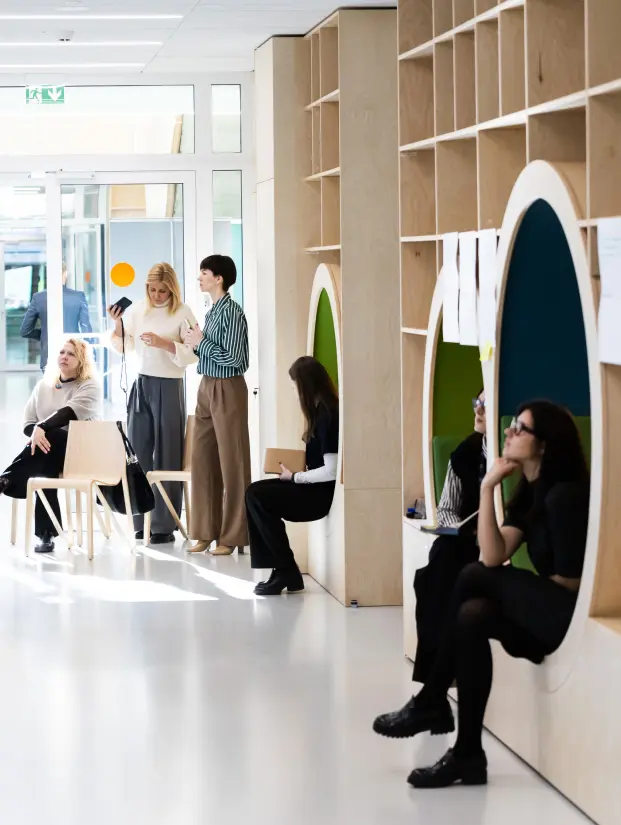 People interact and work in a bright modern study space with wooden shelving and integrated seating alcoves. The informal environment illustrates a KTU MBA study experience built around collaboration and the exchange of ideas.