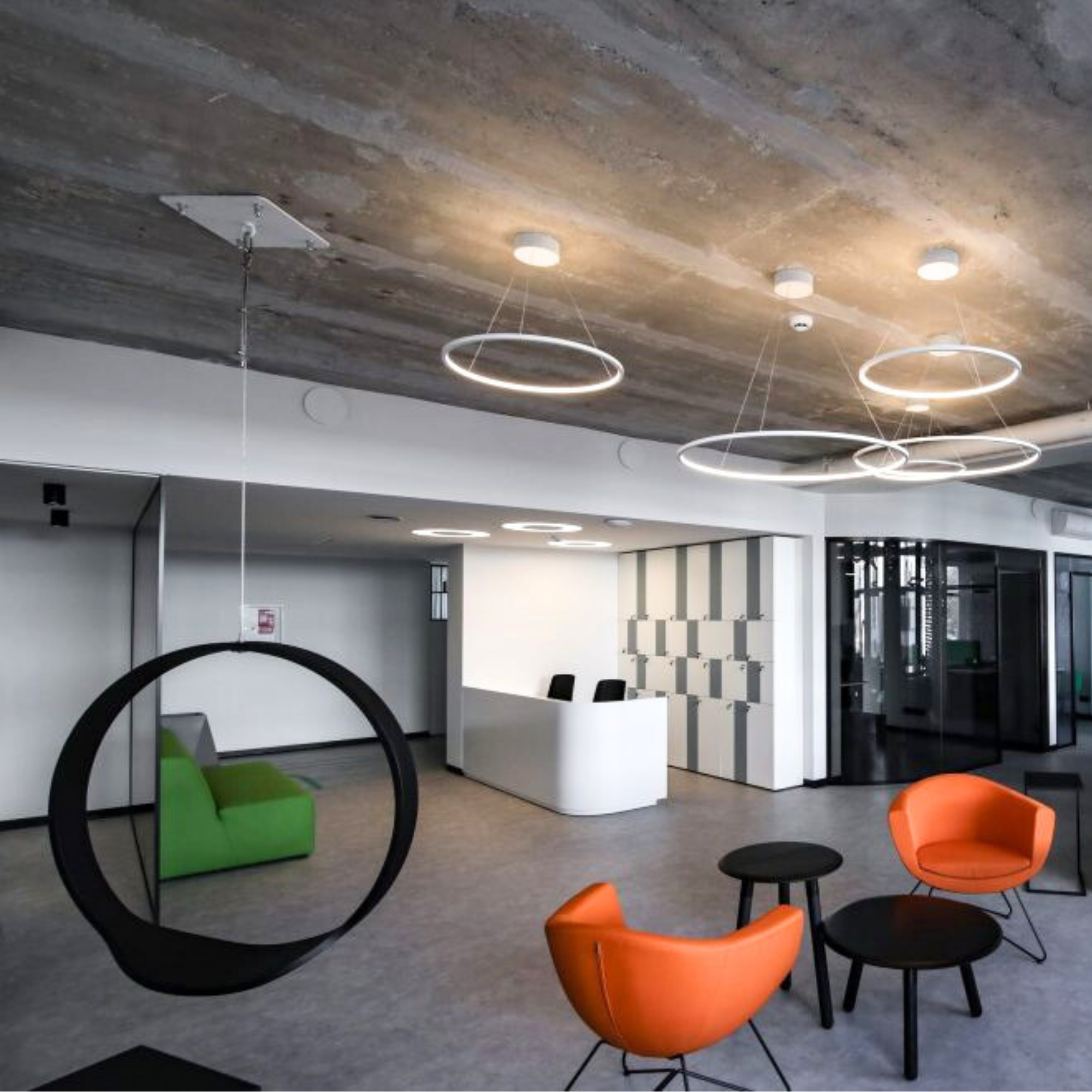 Modern interior of the KTU student information center featuring futuristic ceiling lights, orange and green lounge chairs, and a white reception desk in the background. The space is designed for student consultations and information services.