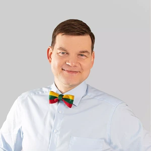 Portrait photo of a man with short brown hair, wearing a light blue shirt and a bow tie in the colors of the Lithuanian flag. He is looking at the camera and smiling, with a neutral greyish background.