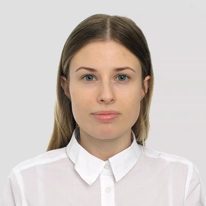 Young woman with straight light brown hair, wearing a white collared shirt, looking directly at the camera against a gray background.