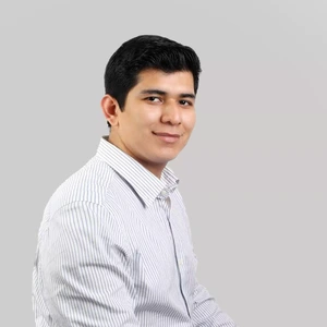Young man with short dark hair, wearing a white striped shirt, looking at the camera with a slight smile, against a gray background.