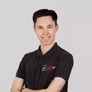 Young man with dark hair, wearing a black polo shirt with the KTU "gifted" logo, smiling and standing with arms crossed against a light background.