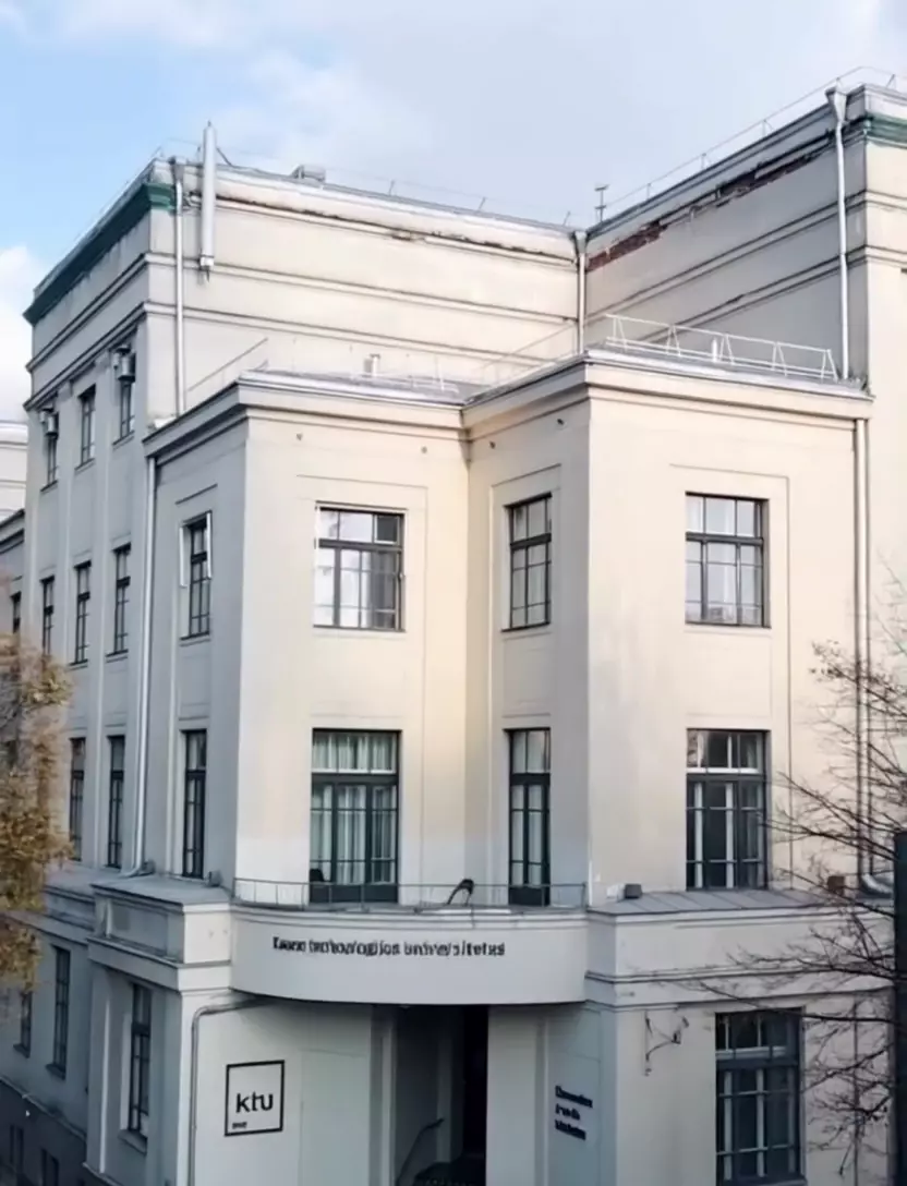 The view above Gedimino Street in central Kaunas drifts slowly toward a pale four‑storey corner block building. From an elevated angle the camera gently closes in highlighting the symmetrical façade of KTU School of Economics and Business with vertical ribbon windows minimalist stone portico and the crisp lines typical of interwar Kaunas modernism.