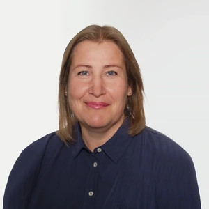 Portrait of Aistija Vaišnorienė smiling at the camera. She has straight, shoulder-length light brown hair and is wearing a navy blue button-up shirt against a plain white background.