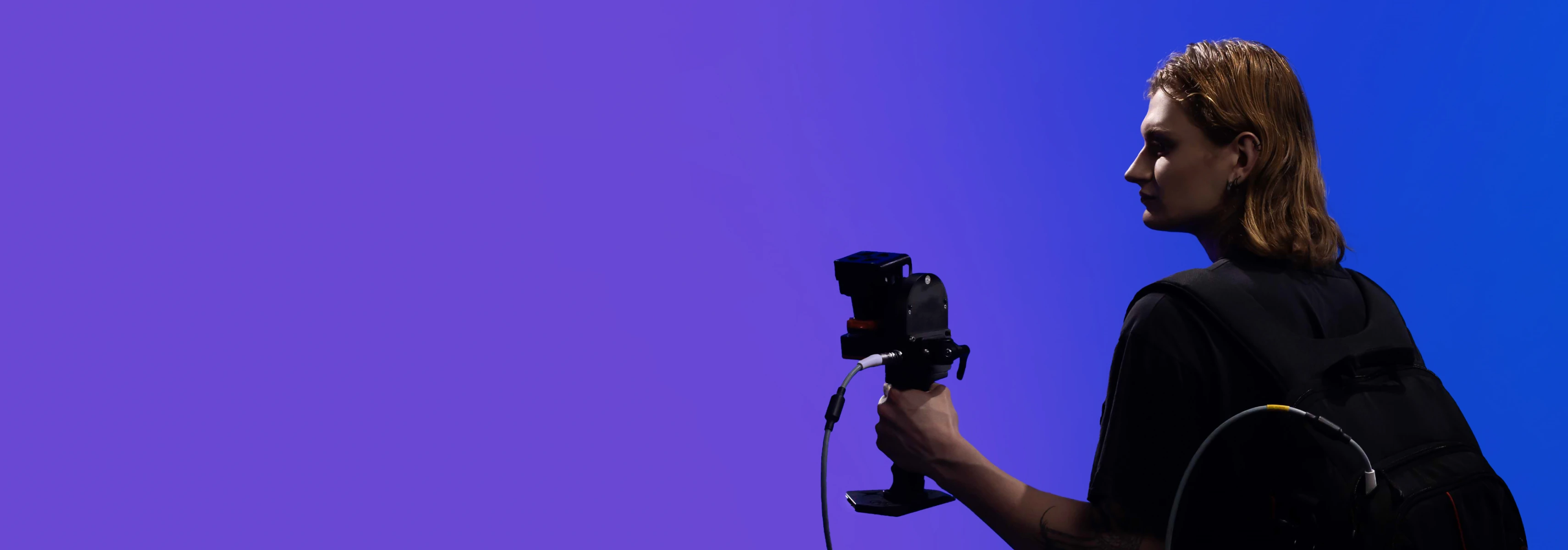 A person stands against a blue background filming with a video camera and stabilizer suitable for civil engineering and architecture research.