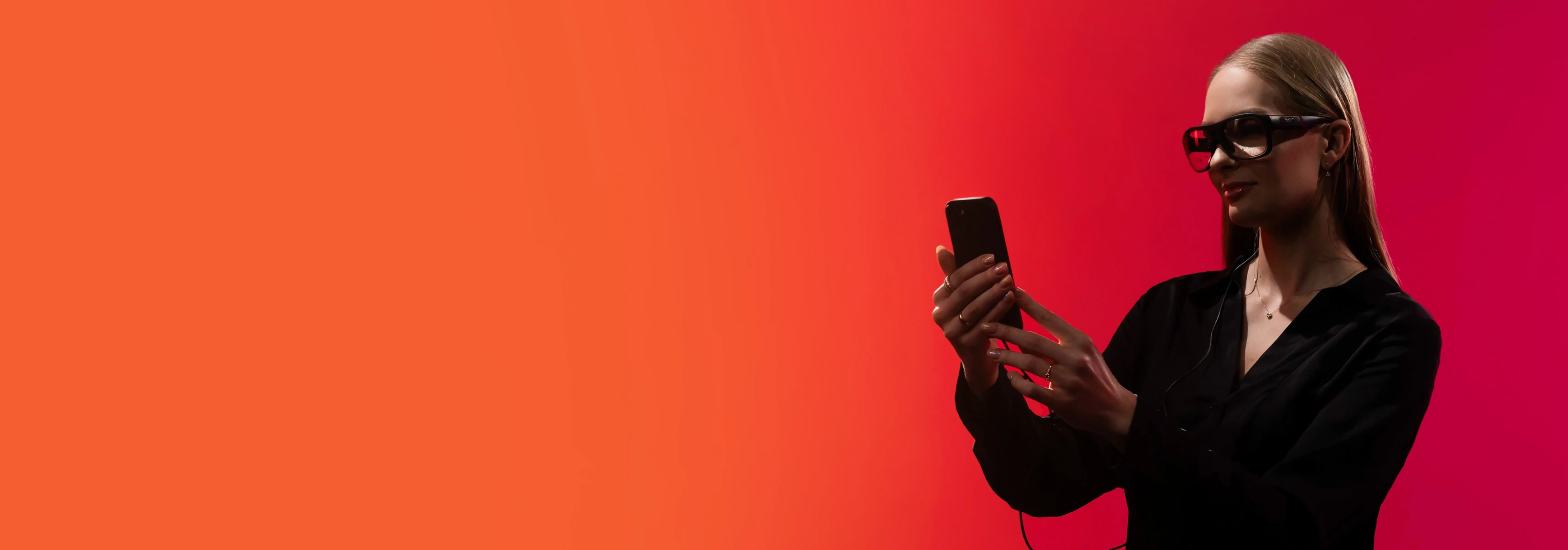 A young woman stands against a red background using a smartphone suitable for the activities of the School of Economics and Business.