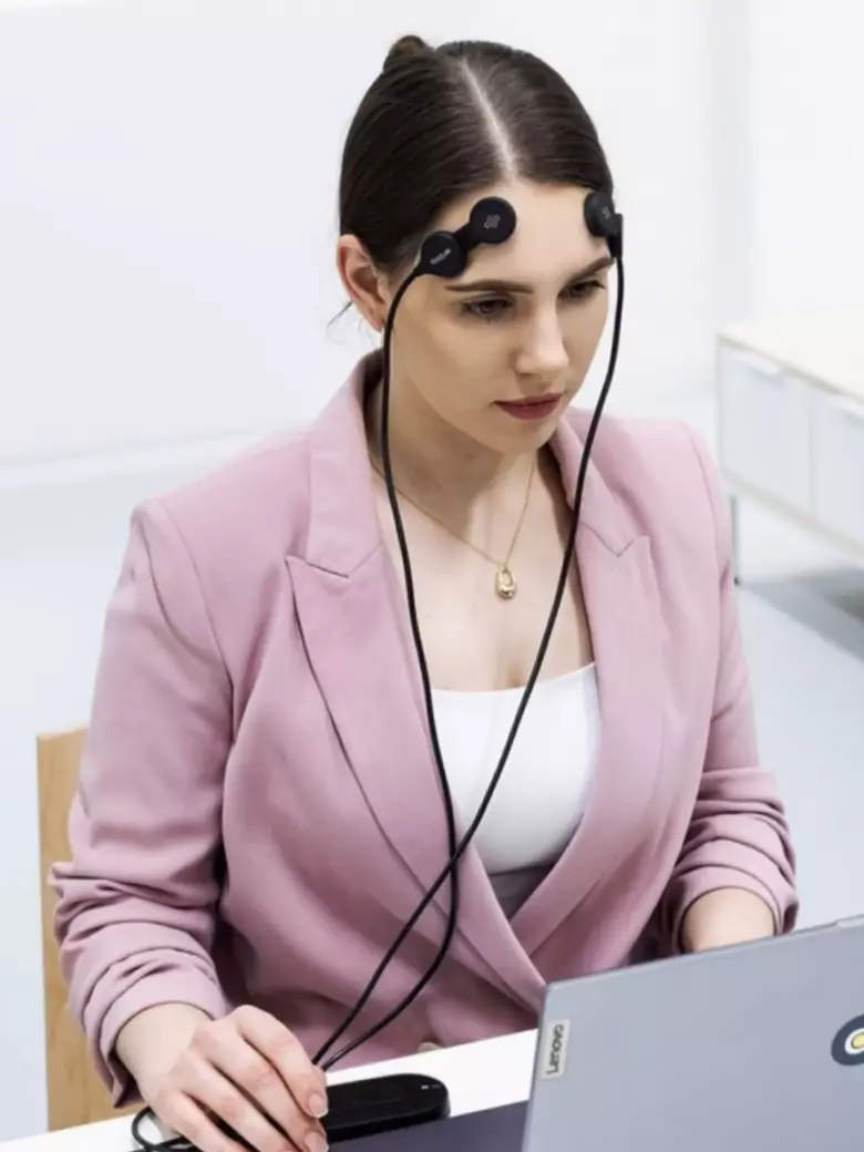 Female PhD student in pink blazer participating in eye tracking research using specialized eye tracking equipment – application of innovative neuroscientific research methods in doctoral studies at Kaunas University of Technology.