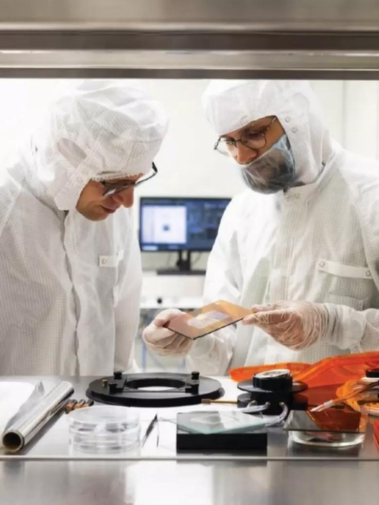 Two scientists in white protective suits discussing research in KTU laboratory while examining samples – doctoral studies scientific research environment at Kaunas University of Technology.