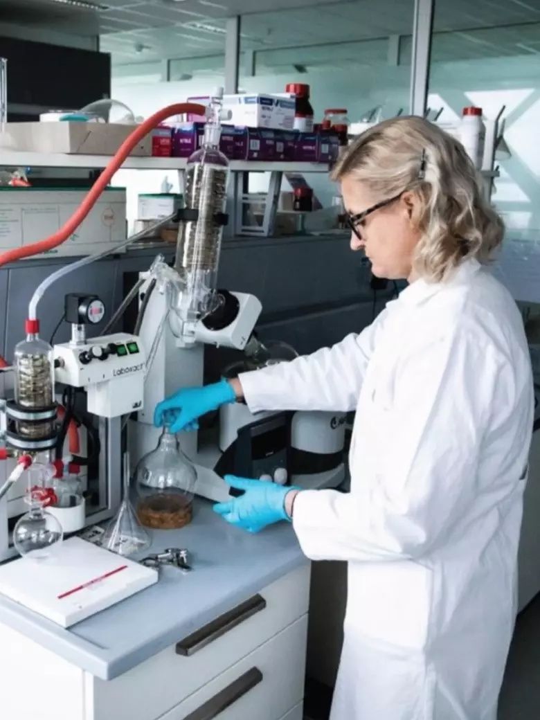 Female PhD student in laboratory attire conducting precise experimental research with microscope and specialized equipment in KTU laboratory – practical doctoral studies competencies and career prospects at Kaunas University of Technology.