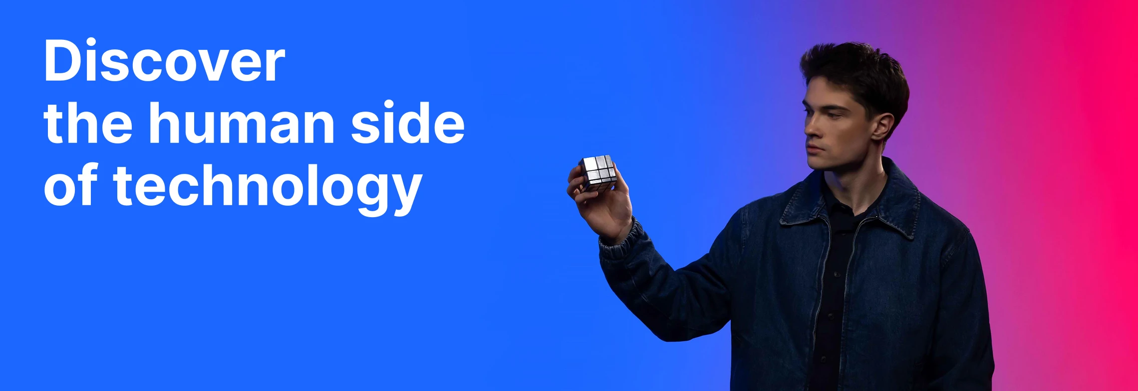 A young man holding a Rubik&rsquo;s cube against a blue-to-pink gradient background alongside the text 'Discover the human side of technology'