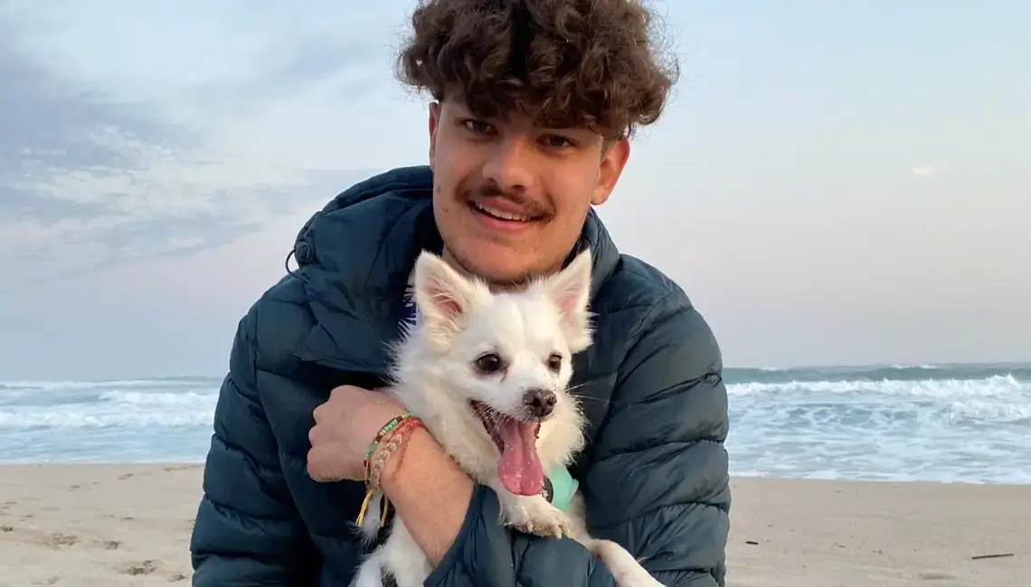 Johannes Coetsee, a student from Cape Town in South Africa, sitting on the beach holding his white small dog.