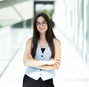 Raminta Šulcė Raminta Šulcė stands with her arms crossed in a bright modern interior. She wears a light grey waistcoat, has long dark hair and glasses, and smiles while looking directly at the camera. Contact Raminta for a consultation about MBA studies.